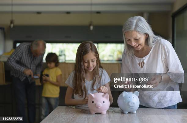 enkelin und großmutter sparen geld in sparschwein spaß und lächelnd - couple saving piggy bank stock-fotos und bilder