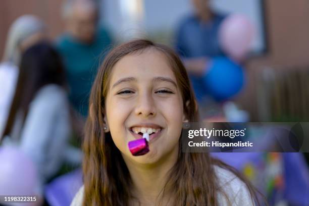 beautiful little girl with a party horn blower smiling at camera with a toothy smile while family stands at background celebrating - party horn blower imagens e fotografias de stock