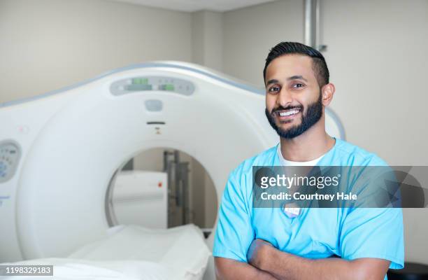 young adult radiologist smiles while standing next to ct machine - mri technician stock pictures, royalty-free photos & images