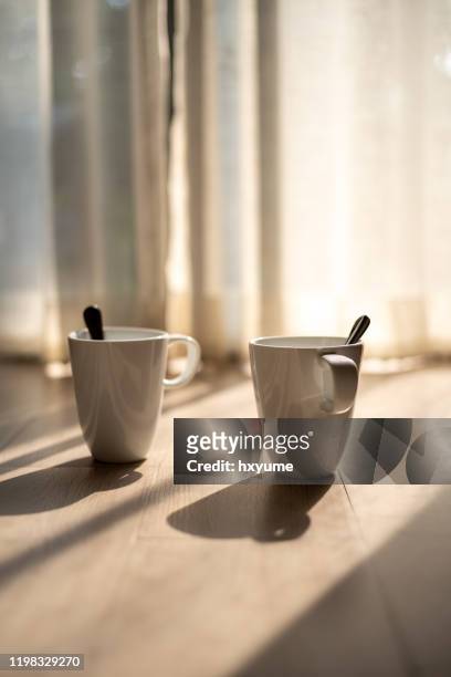 two white mugs with spoon on floor with strong window light - enjoying coffee cafe morning light stock pictures, royalty-free photos & images