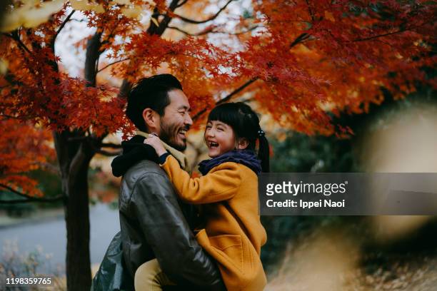father holding cheerful little girl under autumn leaves, tokyo, japan - child hugging tree stock pictures, royalty-free photos & images