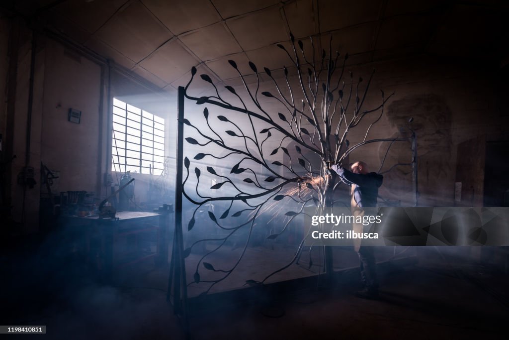 Blacksmith artist working in his smithy studio creating a gate-tree