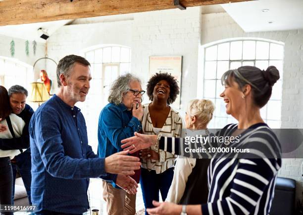 mature friends greeting each other at social gathering - großzügigkeit stock-fotos und bilder
