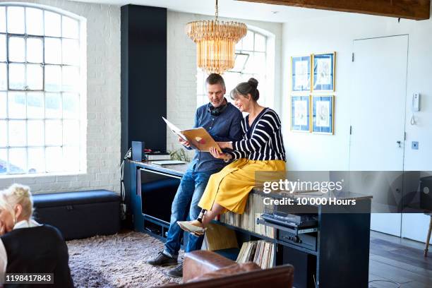 mature couple looking at vinyl record in stylish flat - album fotos fotografías e imágenes de stock