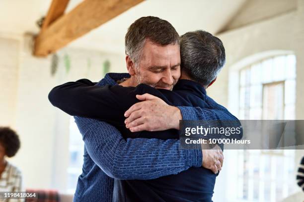 portrait of mature friends embracing with arms around each other - embracing stock pictures, royalty-free photos & images