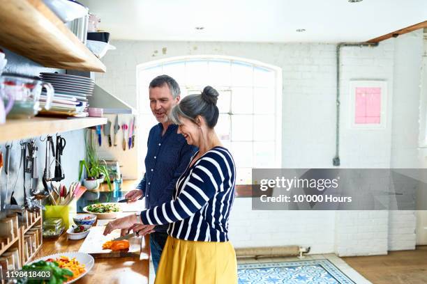 mature couple preparing vegetarian meal in stylish kitchen - kochen stock-fotos und bilder