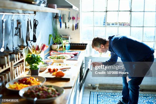 mature man cooking meal and looking in oven - serving dish stock pictures, royalty-free photos & images