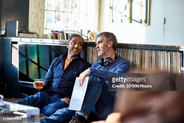 mature male friends sitting together listening to records - friends chatting mature foto e immagini stock
