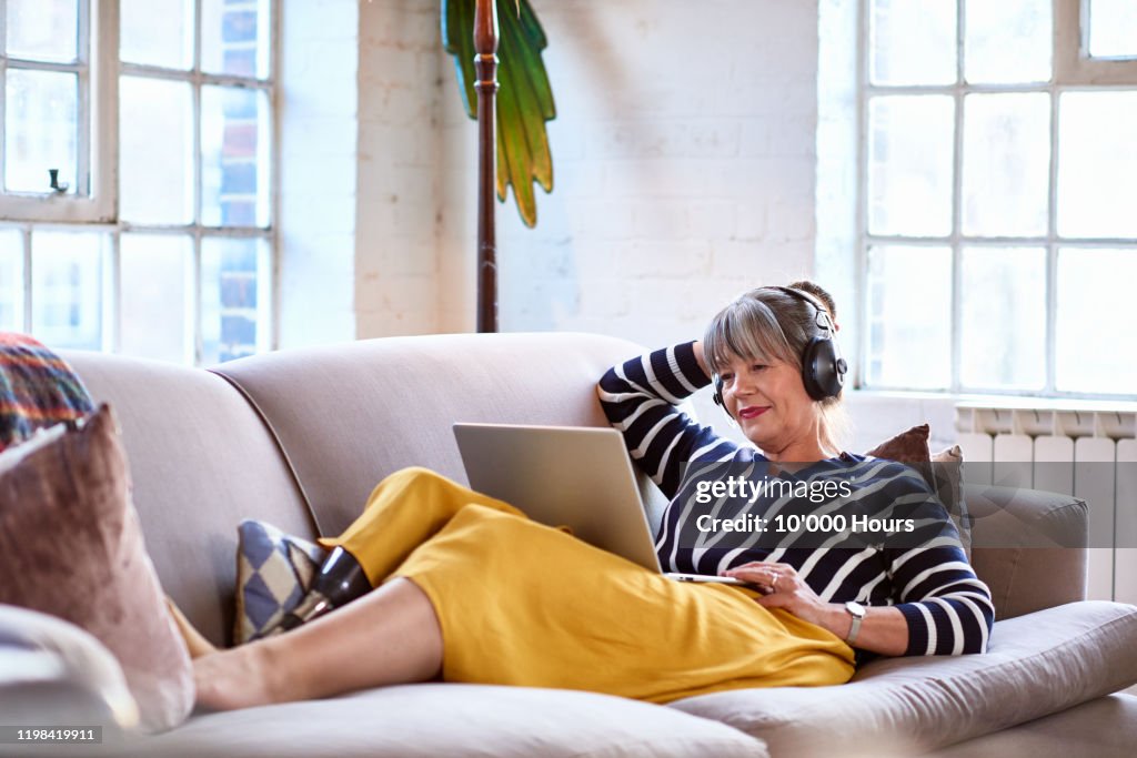 Senior woman wearing headphones watching movie on laptop