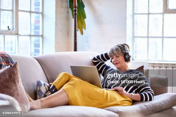 senior woman wearing headphones watching movie on laptop - headphones woman stock-fotos und bilder