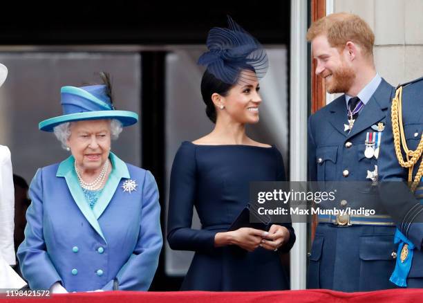 Queen Elizabeth II, Meghan, Duchess of Sussex and Prince Harry, Duke of Sussex watch a flypast to mark the centenary of the Royal Air Force from the...