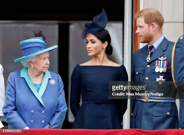 Queen Elizabeth II, Meghan, Duchess of Sussex and Prince Harry, Duke of Sussex watch a flypast to mark the centenary of the Royal Air Force from the...