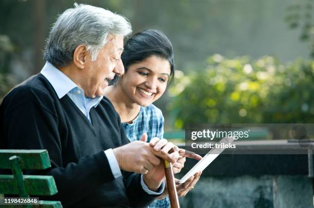 woman with old father using digital tablet at park - retirement community staff stock pictures, royalty-free photos & images