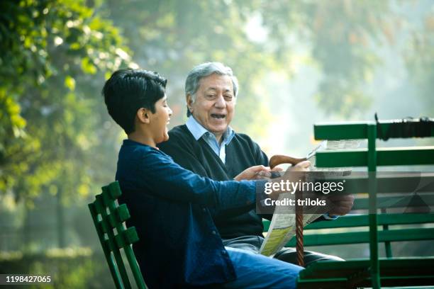 nonno con nipote che si diverte a leggere il giornale al parco - nonni bastone foto e immagini stock