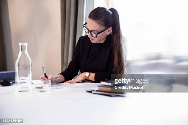 businesswoman writing on documents while sitting by desk at law firm - law firm stock pictures, royalty-free photos & images