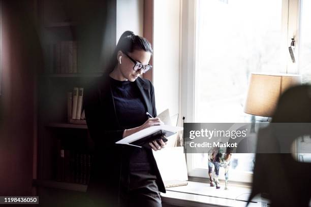 female professional writing on documents while standing by window at law firm - legal counsel stock pictures, royalty-free photos & images