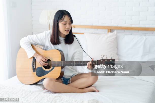 asian teenage girl playing acoustic guitar and singing with happiness on the bedroom at home. girl love music concept. - girls bedroom stock pictures, royalty-free photos & images