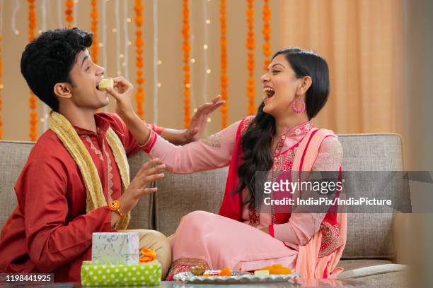 sister stuffing barfi in brother's mouth - rakhi stock pictures, royalty-free photos & images