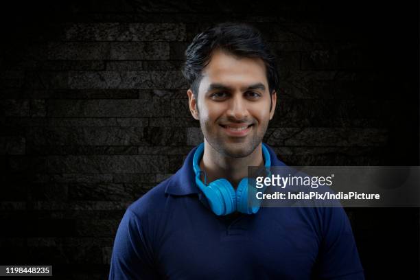 portrait of smiling man with headphones on neck over black background - headphone man on neck stock-fotos und bilder