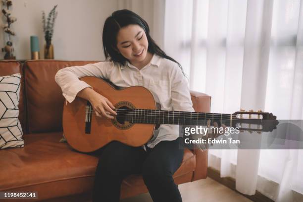 1 asian chinese female playing guitar in living room on sofa - classical guitarist stock pictures, royalty-free photos & images