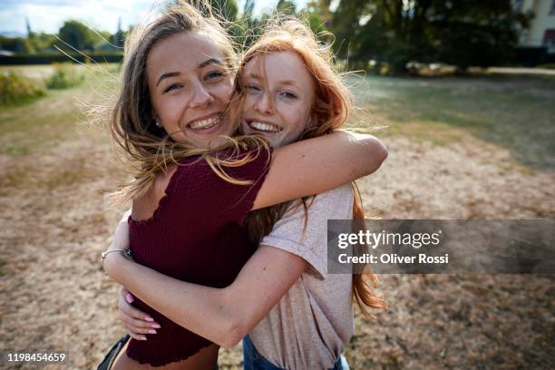 portrait of happy affectionate girlfriends hugging in a park - tossing hair facing camera woman outdoors stock-fotos und bilder
