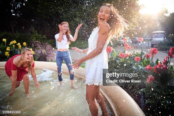 carefee girlfriends splashing with water in a fountain - girls in wet dresses stock-fotos und bilder