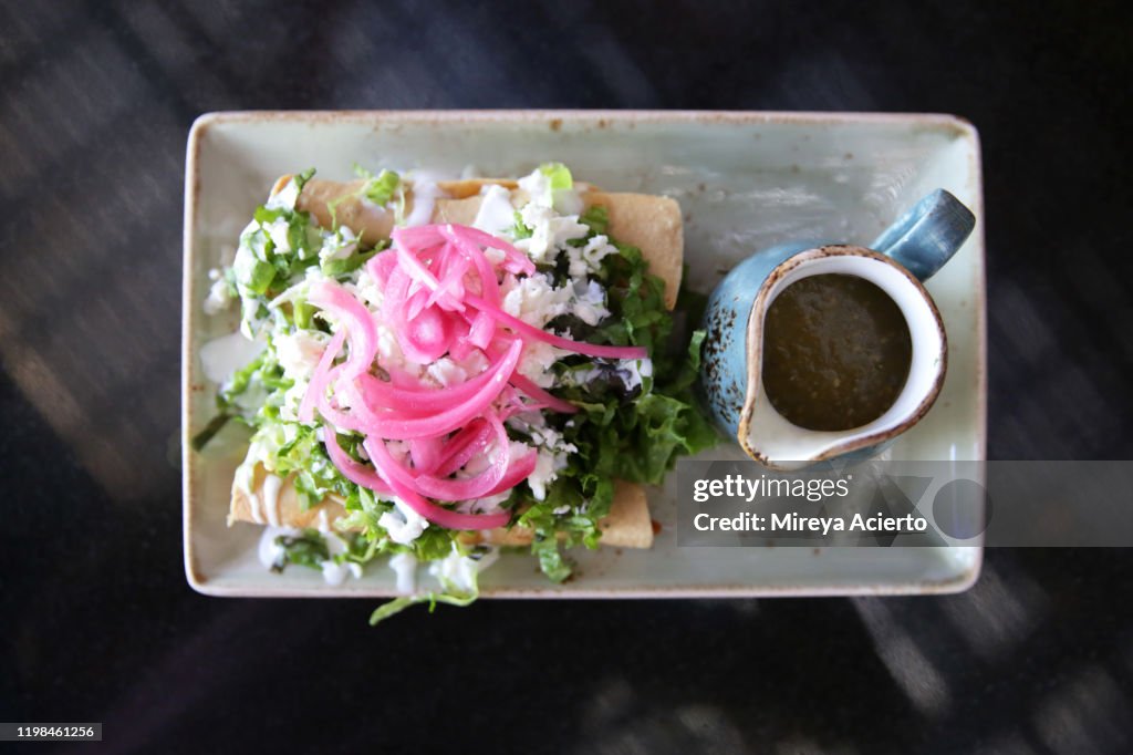 A traditional Mexican dish of chicken flautas served with red onions, lettuce and a side of green salsa.