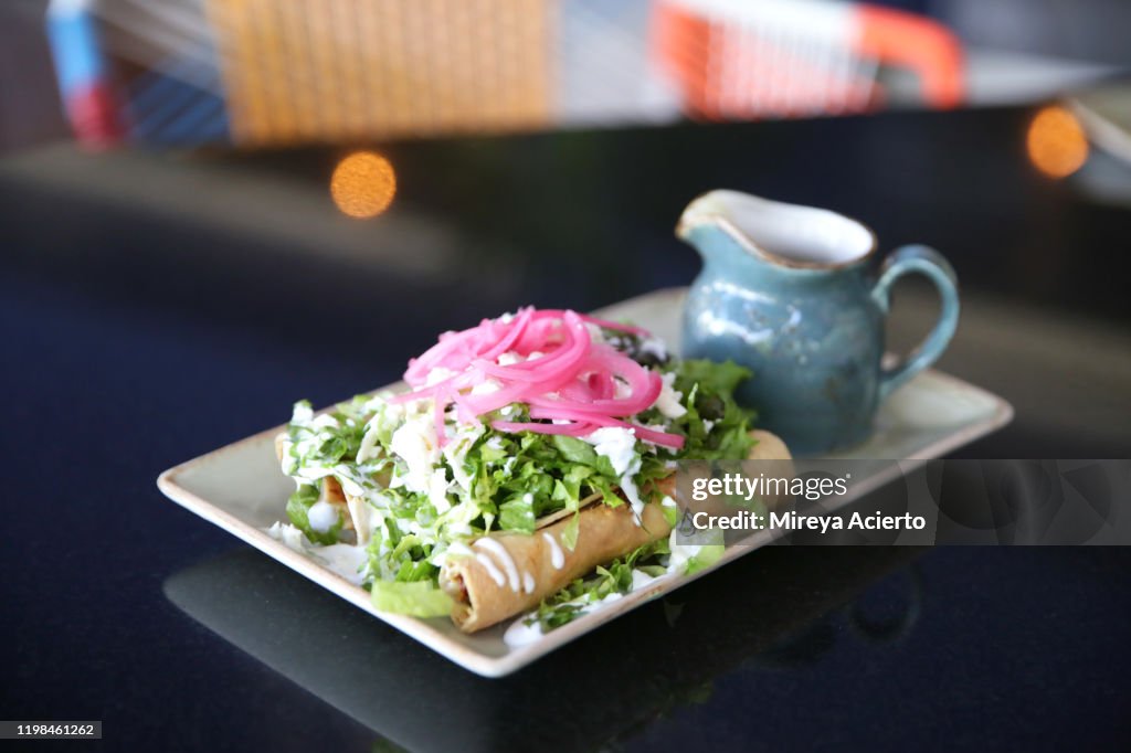 A traditional Mexican dish of chicken flautas served with red onions, lettuce and a side of green salsa.
