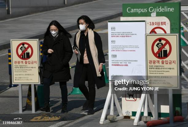 People wearing face masks walk past a 'no tourists' sign amid concern over the spread of the SARS-like virus, at the main entrance of a university in...