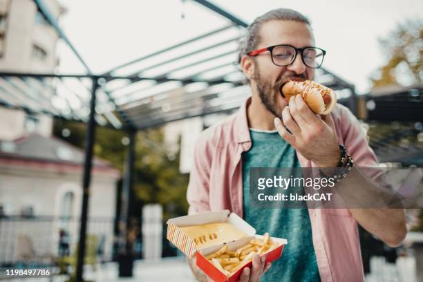 o homem novo está comendo o cão quente - hot dog - fotografias e filmes do acervo