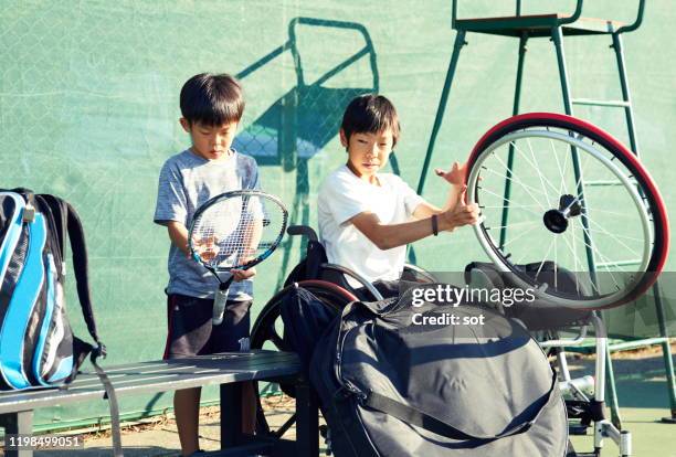 young boy in a wheelchair with his younger brother both preparing to play tennis - wheelchair tennis stock pictures, royalty-free photos & images