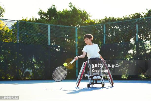 young boy in a wheelchair playing tennis on a tennis court - japanese tennis stock pictures, royalty-free photos & images