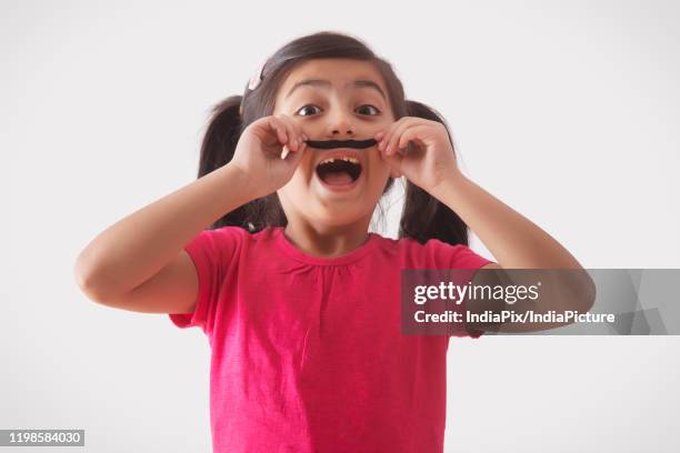 portrait of a young girl wearing fake moustache and smiling - fake of indian girls stock pictures, royalty-free photos & images