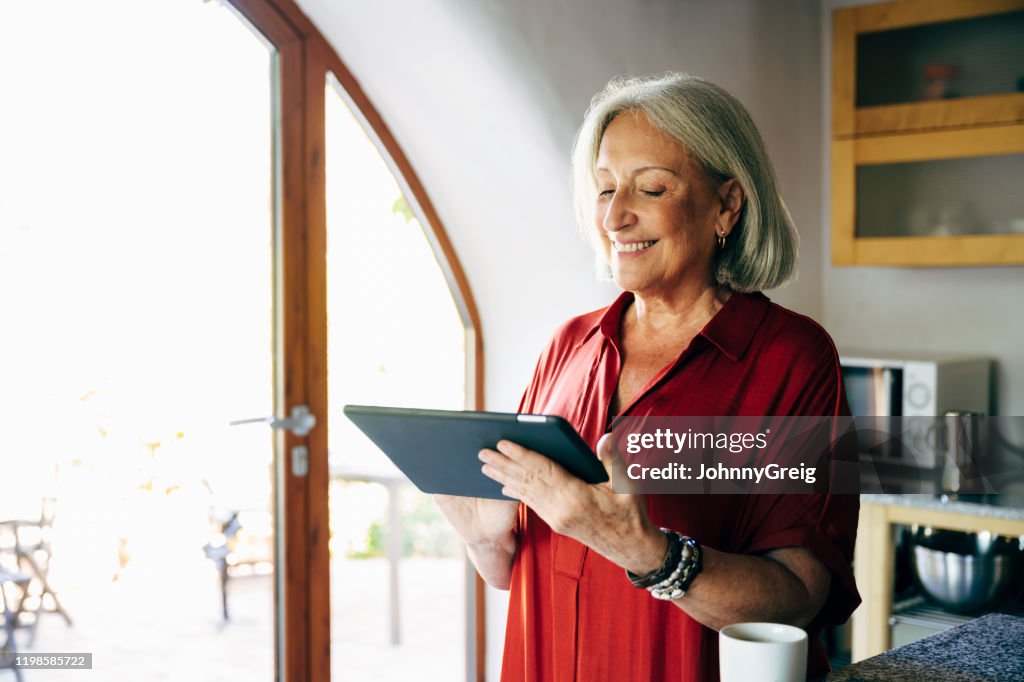 Mujer de alto rango sonriente española usando tableta digital en casa