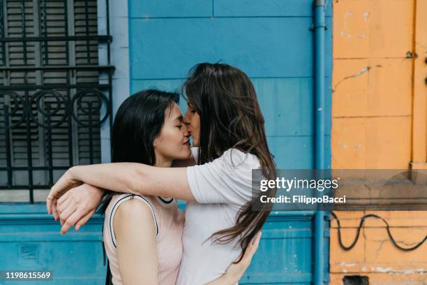 young adult couple embracing and kissing against a blue and orange wall - first kiss imagens e fotografias de stock