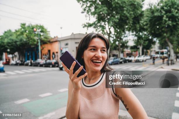 young adult woman sending a voice message with her smartphone - conference phone stock pictures, royalty-free photos & images