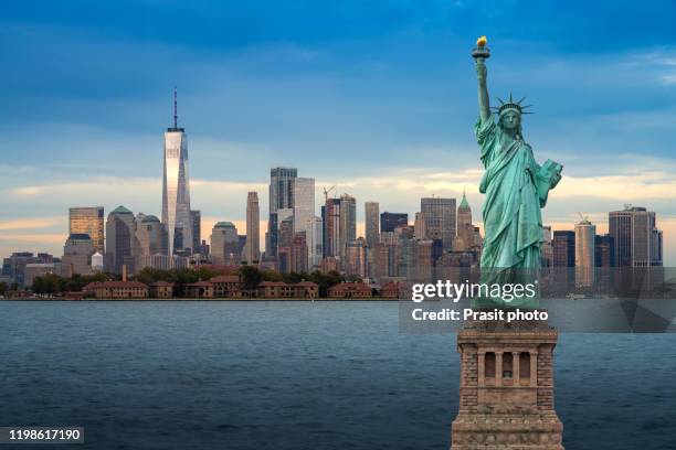 the statue of liberty with downtown new york skyline panorama with ellis island in the foreground at night in new york city, usa. - statue of liberty new york city - fotografias e filmes do acervo