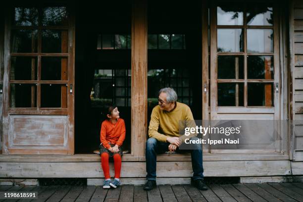 grandfather and granddaughter sitting on patio and smiling at each other - asian young stock pictures, royalty-free photos & images