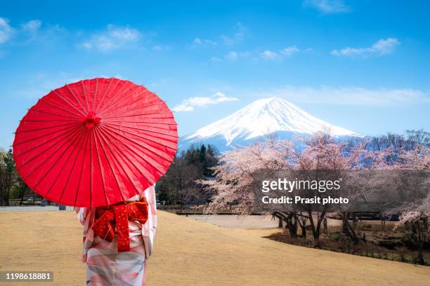 asian young woman traveller wearing japanese traditional kimono with red umbrella sightseeing at famous destination mt. fuji and cherry blossom full blooming at yagizaki park in spring season in yamanashi, japan. - mt fuji stockfoto's en -beelden