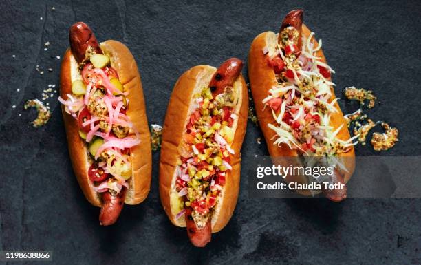 three gourmet hot dogs on black background - hotdog stockfoto's en -beelden