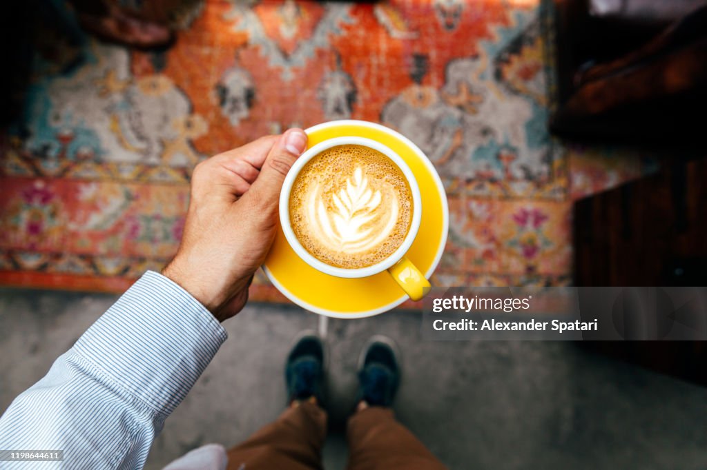 Man holding yellow cup with cappuccino, personal perspective view