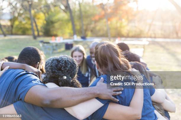 vrijwilligers huddle together en tonen eenheid - briefing stockfoto's en -beelden