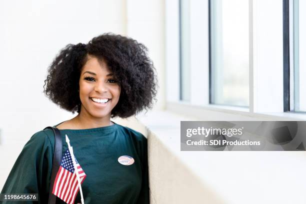 smiling mid adult woman holding flag and wearing sticker - women politics stock pictures, royalty-free photos & images