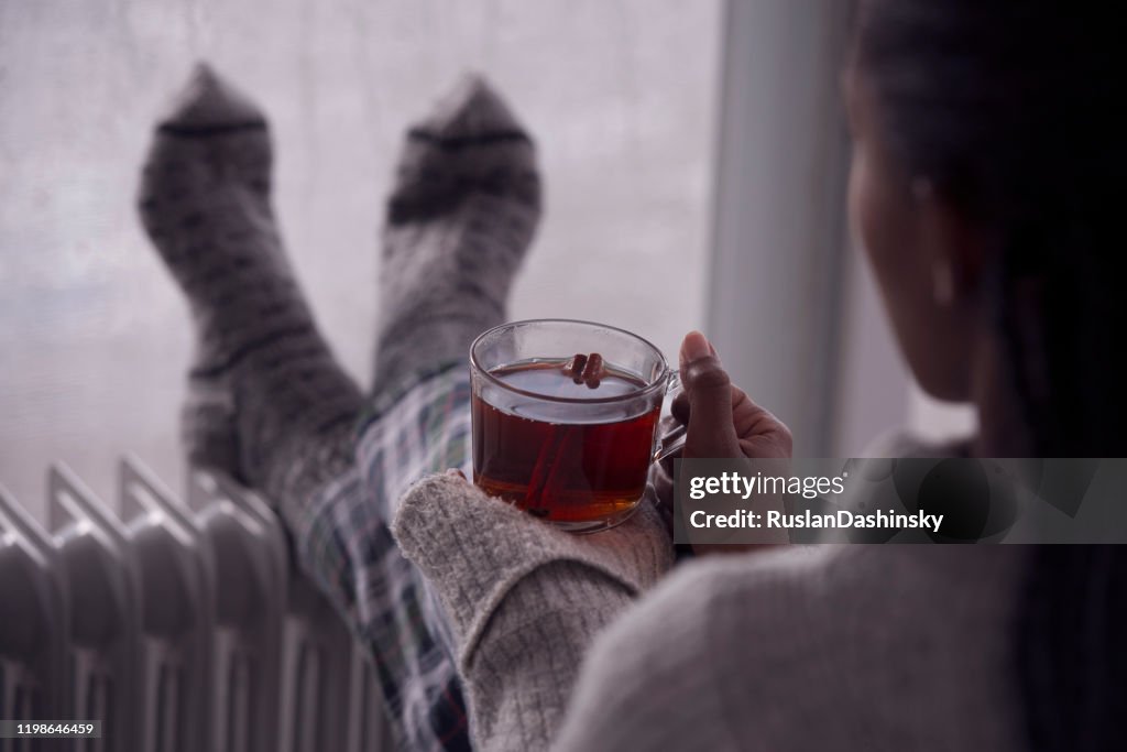 Over het schouder beeld van een vrouw die thee thuis drinkt in koud en nat weer.