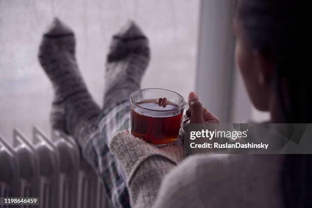 over het schouder beeld van een vrouw die thee thuis drinkt in koud en nat weer. - scorches stockfoto's en -beelden