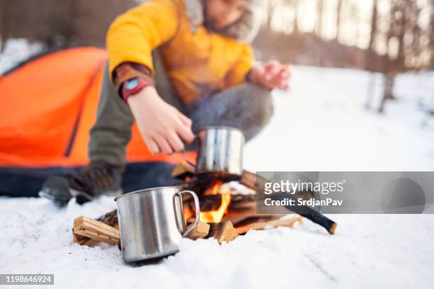 jongen koken thee op een kampvuur - haardvuur stockfoto's en -beelden