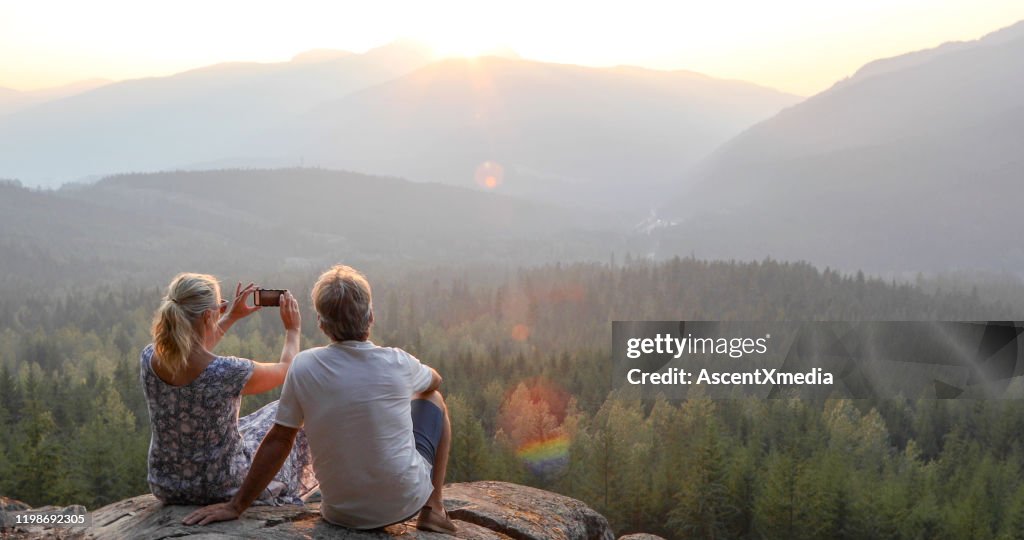 Mature couple relax on mountain ledge, look out to view