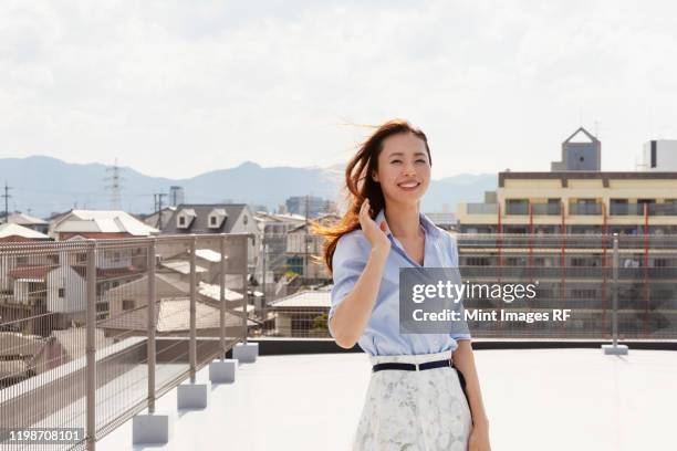 young japanese woman standing on a rooftop in an urban setting, looking at camera. - 女性　日本人　笑顔　30代 ストックフォトと画像