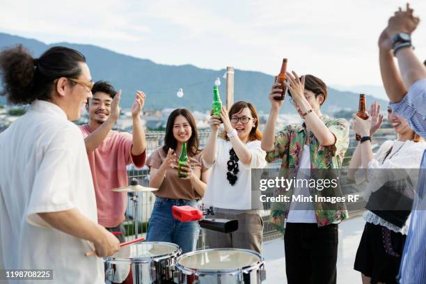 smiling group of young japanese men and women standing on a rooftop in an urban setting, drinking beer. - man sipping beer smiling stockfoto's en -beelden
