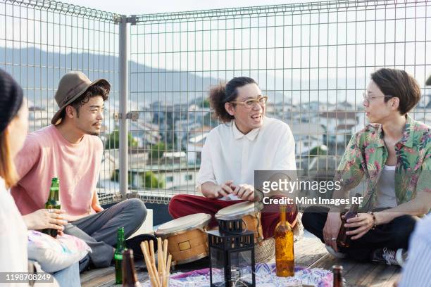 group of young japanese men and women sitting on a rooftop in an urban setting, drinking beer. - slagverksinstrument bildbanksfoton och bilder